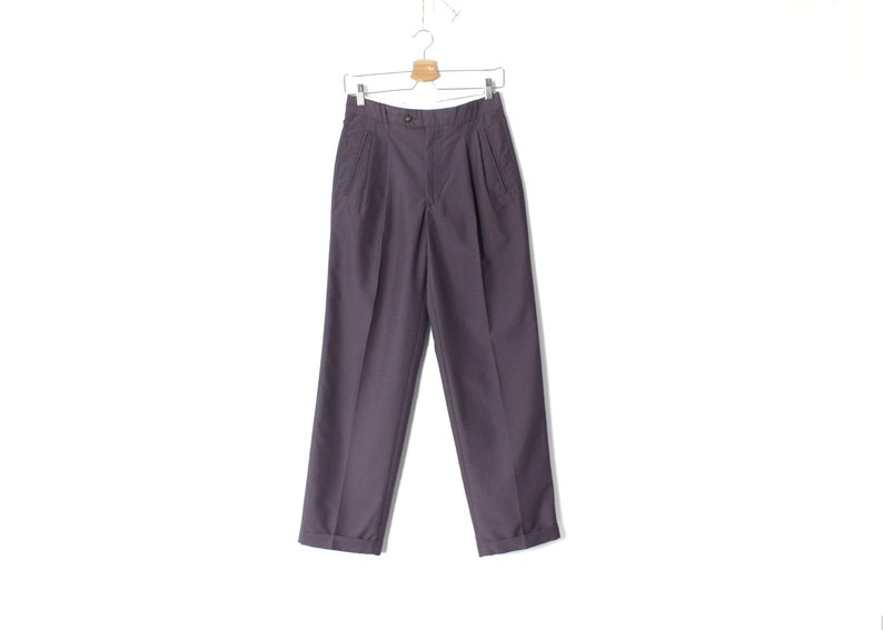 Puede incluir: Un pantal&oacute;n gris oscuro con pliegues colgado de una percha blanca sobre un fondo blanco.