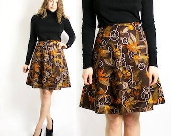 Könnte beinhalten: Ein brauner und orangefarbener A-Linienrock mit Blumenmuster und einem schwarzen Rollkragenpullover. Der Rock hat ein wirbelndes Muster mit braunen, orangefarbenen und weißen Akzenten.
