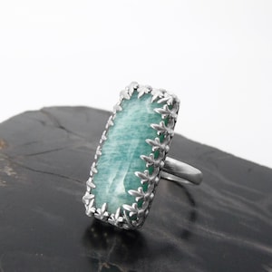 May include: A silver ring with a large, rectangular, light green gemstone set in a silver filigree design.
