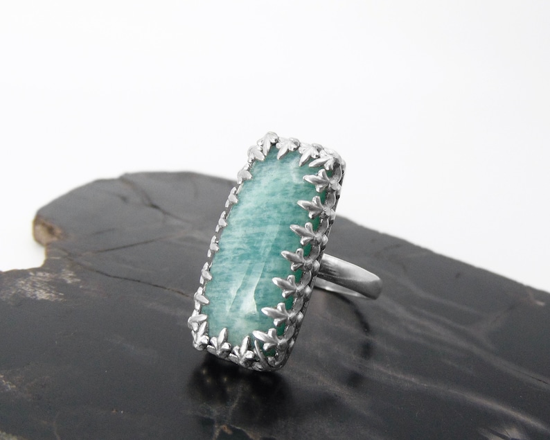 May include: A silver ring with a large, rectangular, light green gemstone set in a silver filigree design.