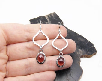 Puede incluir: Un par de pendientes de plata con un diseño en forma de lágrima y un colgante redondo de piedra roja.
