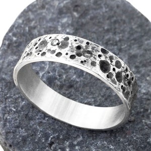 May include: A silver band ring with a textured surface that resembles the moon's surface.