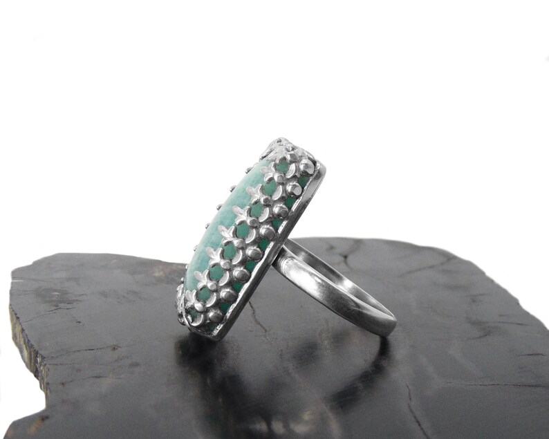 May include: A silver ring with a green gemstone set in a decorative floral design.