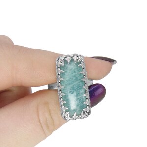 May include: A silver ring with a rectangular green gemstone set in a detailed silver frame.