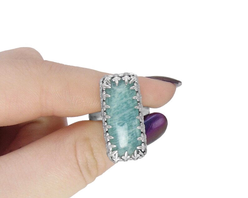 May include: A silver ring with a rectangular green gemstone set in a detailed silver frame.