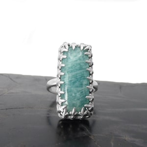 May include: A silver ring with a rectangular green gemstone set in a decorative silver frame.