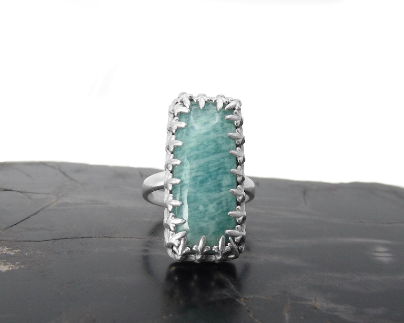 May include: A silver ring with a rectangular green gemstone set in a decorative silver frame.