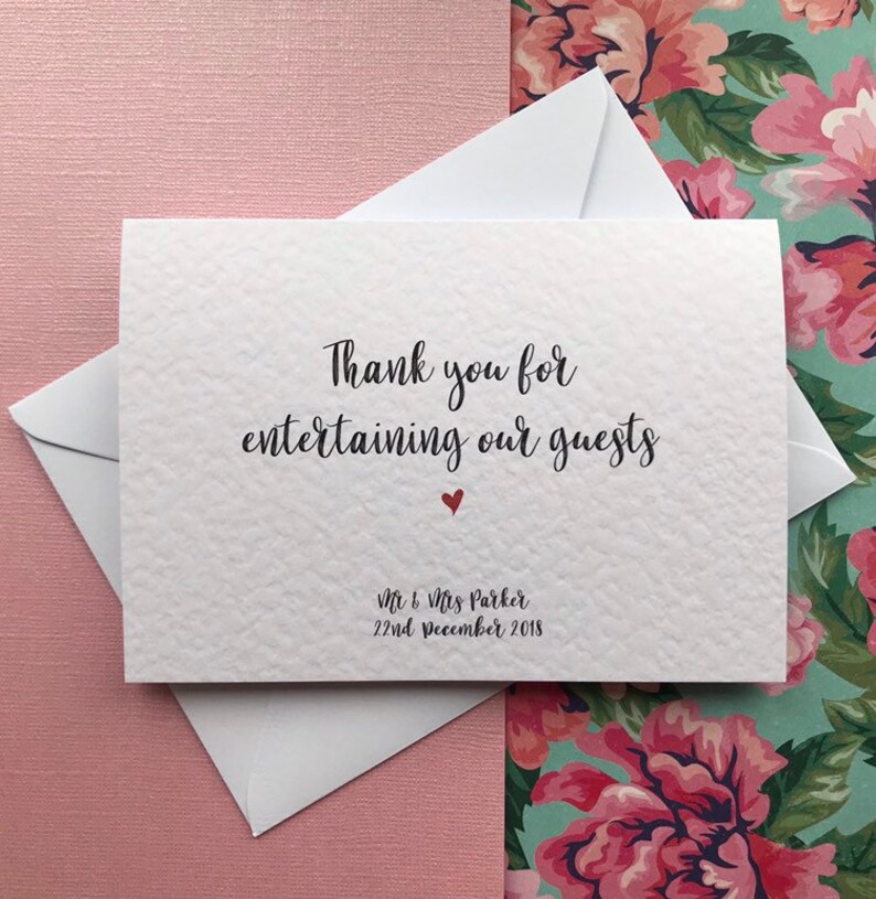 May include: White thank you card with the text "Thank you for entertaining our guests" in black cursive font. A small red heart is below the text. The text "Mr & Mrs Parker 22nd December 2018" is printed in black at the bottom of the card.