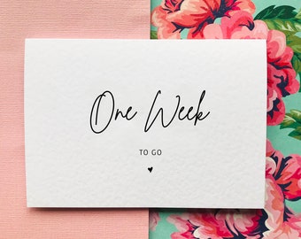 May include: White card with black text that reads "One Week To Go" with a small heart symbol below the text.