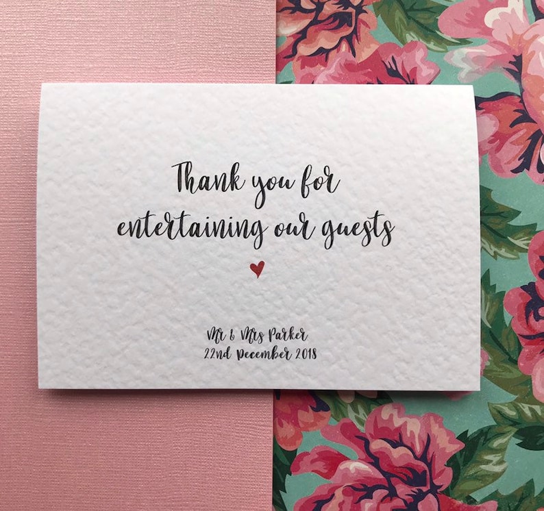 May include: White card with black text that says "Thank you for entertaining our guests" with a small red heart below the text. The text "Mr & Mrs Parker 22nd December 2018" is printed in black at the bottom of the card.