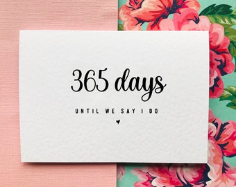 May include: White card with black text that reads "365 days until we say I do" with a small heart symbol.