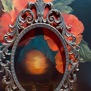 May include: An ornate oval-shaped picture frame with a dark bronze finish. The frame has intricate scrollwork and floral designs.