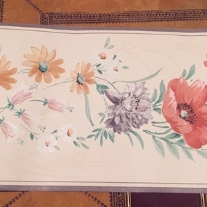 May include: Floral wallpaper border featuring a repeating pattern of watercolor flowers. The design includes red poppies, orange daisies, and purple chrysanthemums, with green leaves and stems on a cream background.