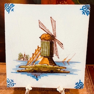Peut inclure: Un carreau de céramique blanc avec une bordure bleue et blanche. Le carreau présente une image peinte à la main d'un moulin à vent sur une petite île dans un plan d'eau.