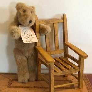 Puede incluir: Un oso de peluche marrón claro con una etiqueta que dice "The Teddy Collection, Bumba Bear, Billy Bear" está de pie junto a una pequeña silla de madera pintada de amarillo. La silla tiene un respaldo y un asiento de listones.