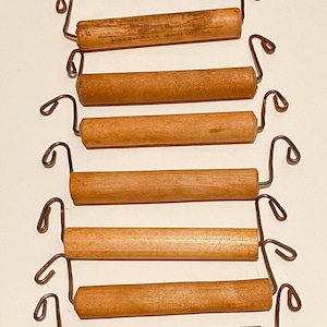 May include: Six wooden dowel rods with metal hooks on each end. The rods are all the same size and are arranged in a vertical stack. The top rod has the text "ACME HANDLE CO. JERSEY CITY, N.J." printed on it.