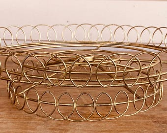 May include: A gold metal tiered cake stand with a circular design. The stand is made of wire and has a delicate, intricate pattern.