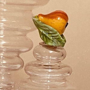 Puede incluir: Una botella de vidrio transparente con un tapón en forma de pera. El tapón está hecho de cerámica y presenta una pera con hojas verdes.