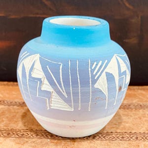 Peut inclure: Un petit pot en céramique bleu et blanc avec un motif géométrique. Le pot est recouvert d'un glacis bleu clair et présente des motifs géométriques blancs gravés à la surface. Le pot est de couleur rose clair au fond.