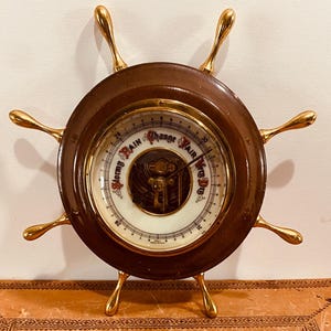 May include: A wooden ship's wheel barometer with a brass rim and spokes. The barometer face has a white background with black markings and the words "Stormy Rain Change Fair Very Dry".