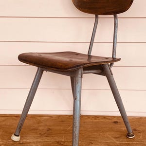 May include: Vintage wooden chair with a curved back and seat. The chair has a dark brown finish on the seat and backrest, with a metal frame in a gray color. The legs have white rubber feet.
