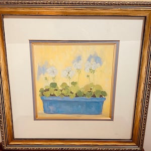 Op de afbeelding: Een ingelijste print van een stilleven met witte bloemen in een blauwe pot op een gele achtergrond.