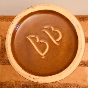 May include: Close-up of the base of a brown ceramic mug with the letters "BB" impressed into the glaze.