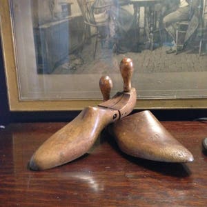 May include: A pair of wooden shoe trees with a hinged design. The shoe trees are brown and have a smooth finish.