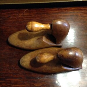 May include: Two wooden shoe trees with a brown finish and a light brown wooden handle. The shoe trees are designed to help maintain the shape of shoes.