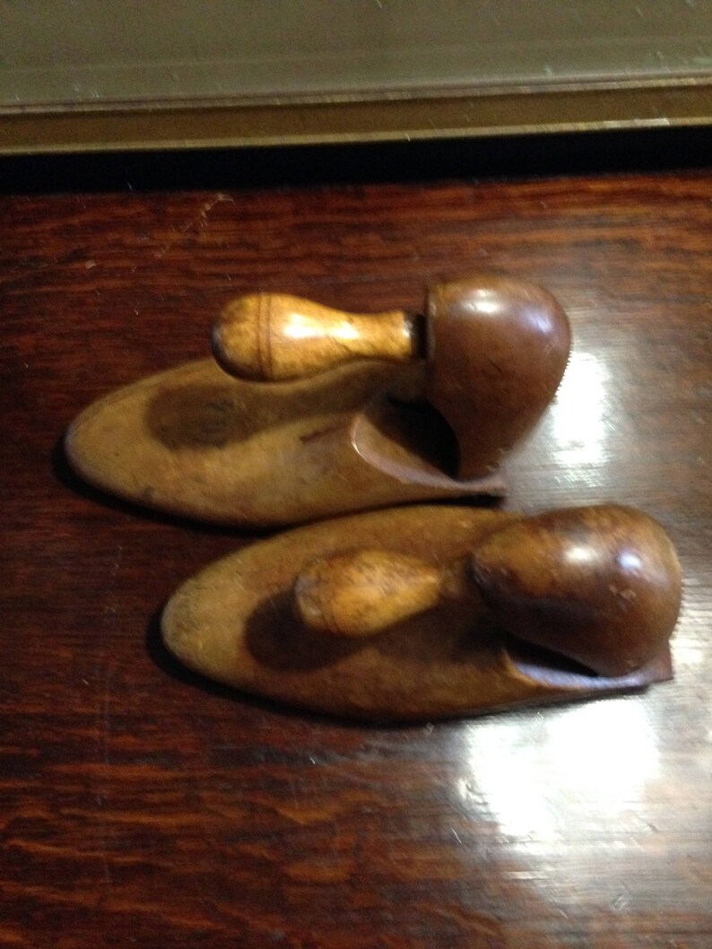 May include: Two wooden shoe trees with a brown finish and a light brown wooden handle. The shoe trees are designed to help maintain the shape of shoes.