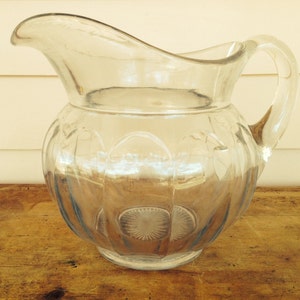May include: A clear glass pitcher with a textured, ribbed design. The pitcher has a wide mouth and a handle.