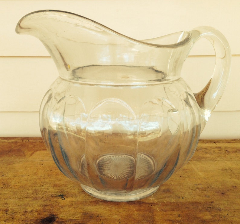 May include: A clear glass pitcher with a textured, ribbed design. The pitcher has a wide mouth and a handle.