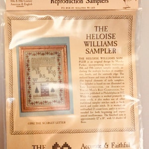 May include: A close-up of packaging for a cross-stitch sampler kit featuring a reproduction of "The Heloise Williams Sampler" by Marsha Parker. The sampler is a traditional 18th and 19th century design with multiple borders of strawberries, hands, and a sawtooth edge. The kit includes 13 shades of floss and is approximately 30.5 cm x 45.7 cm when finished.