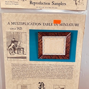 Peut inclure: Une reproduction d'un sampler vintage de table de multiplication datant de 1825 environ. Le sampler est encadré dans un cadre en bois brun et présente un fond blanc avec du texte noir. Le sampler mesure 17,8 cm sur 15,2 cm et est travaillé sur un fil de lin teinté à la main de 35 fils. Le sampler est une reproduction d'une pièce d'une collection privée.