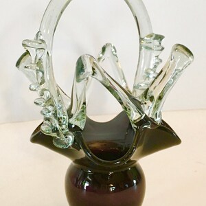 Peut inclure: Un vase en verre transparent avec une base en verre noir et une poignée en verre transparent. Le vase a un design unique et abstrait avec une forme ondulée et organique.