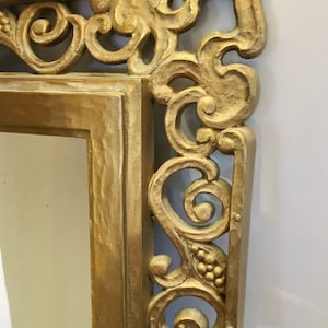 May include: A gold-painted ornate mirror frame with intricate carvings and a scrolled design.
