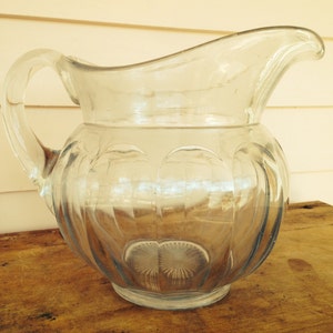 May include: A clear glass pitcher with a textured, ribbed design. The pitcher has a wide mouth and a handle.