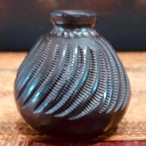 Puede incluir: Un pequeño jarrón de cerámica negro con un patrón de espiral. El jarrón tiene un cuerpo redondeado y un cuello estrecho.