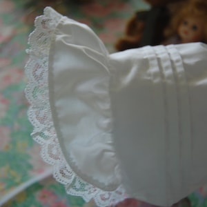 May include: A white bonnet with a lace trim. The bonnet has a ruffled edge and is made of a soft, lightweight fabric.