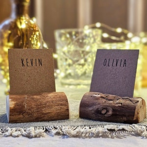 May include: Two rustic wooden place card holders with the names "Kevin" and "Olivia" written on brown paper cards.