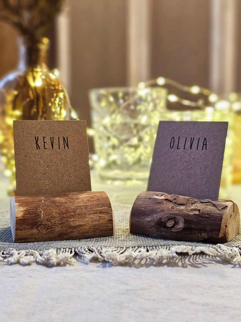 May include: Two rustic wooden place card holders with the names "Kevin" and "Olivia" written on brown paper cards.