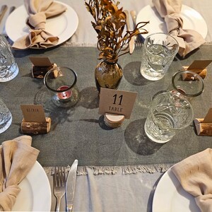 May include: A table setting with a gray tablecloth, white plates, and brown napkins. There are glasses of water, candles, and place cards with names on them. The table number is 11.