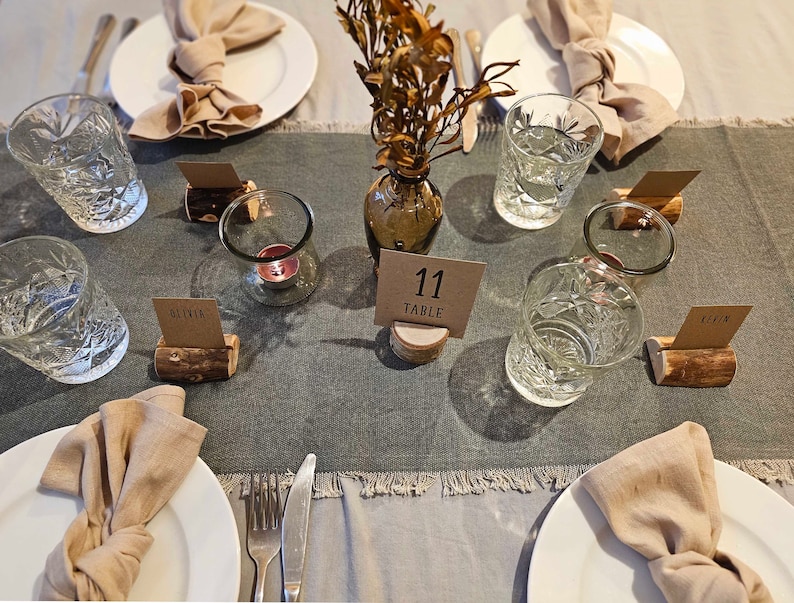May include: A table setting with a gray tablecloth, white plates, and brown napkins. There are glasses of water, candles, and place cards with names on them. The table number is 11.