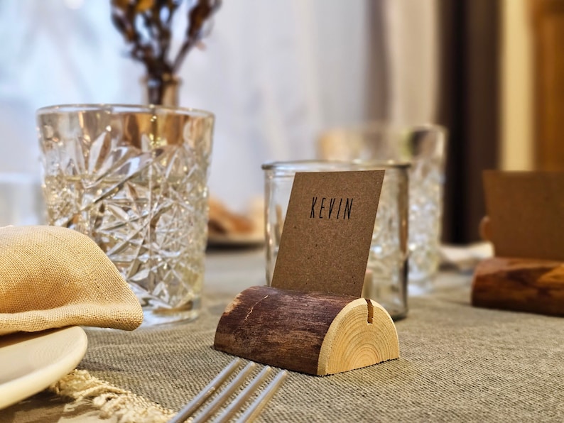 May include: A wooden table number holder with a brown and beige finish. A brown card with the name "Kevin" is displayed in the holder.