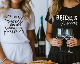 May include: Two women wearing matching white and black t-shirts with text. The white shirt says "I put a spell on him now he's mine" with a ring symbol. The black shirt says "Bride's Witches".