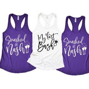 Könnte beinhalten: Drei lila Tanktops mit weißem Text. Der Text auf den linken und rechten Tanktops lautet "Smashed in Nash" mit einer Grafik von zwei Champagnergläsern. Der Text auf dem mittleren Tanktop lautet "My Last Bash" mit einer Grafik eines Rings.