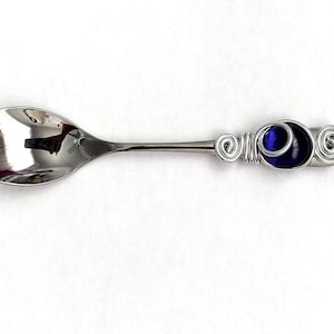May include: A silver teaspoon with a blue glass bead wrapped in silver wire on the handle.