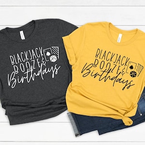May include: Two t-shirts with the text "Blackjack Booze & Birthdays" printed on them. One shirt is dark gray and the other is yellow.