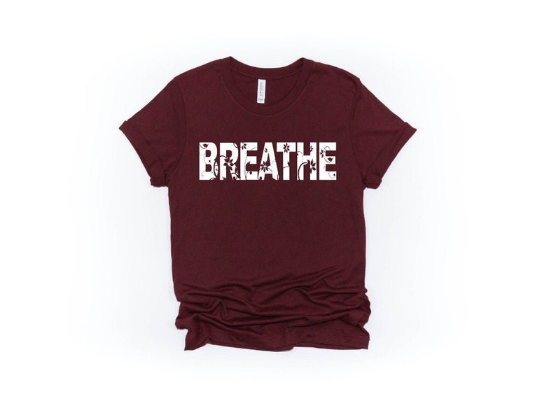 May include: A maroon t-shirt with the word "BREATHE" printed in white on the front. The letters are outlined with a floral design.