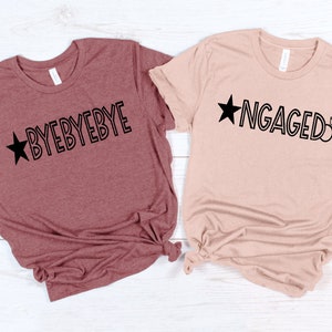 May include: Two t-shirts with a star and text. The maroon shirt says "BYEBYEBYE" and the beige shirt says "ENGAGED" with a diamond ring.